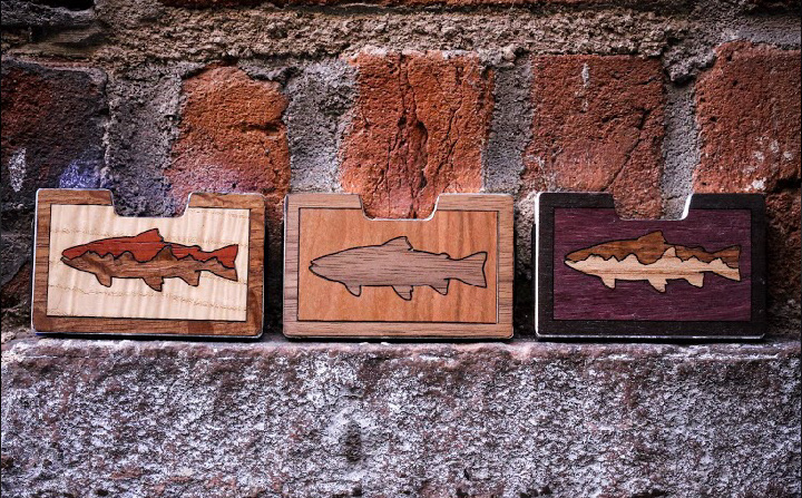 Three trout wood inlay wallet variations displayed against brick