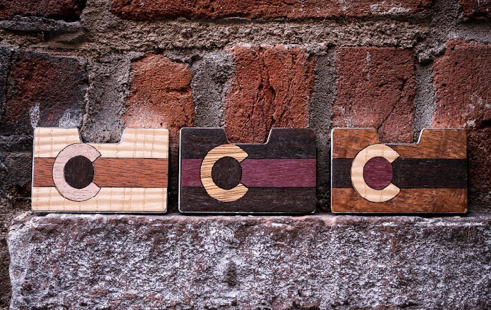 Three Colorado flag wood inlay wallets displayed against a brick wall